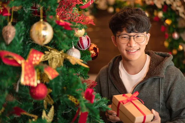 Ázsiai Férfi Pulóverben Mosolyog Kezében Ajándék Míg Díszített Karácsonyfa Csillogó — Stock Fotó