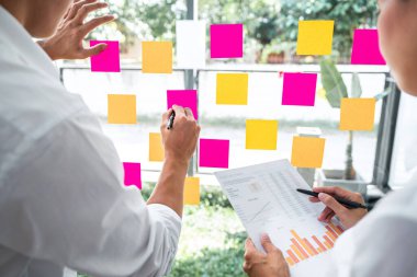 Finansal belge grafiğinde pazarlama büyümesi üzerinde çalışan iş ekibi istatistikleri raporlayarak, cam duvara yapıştırdığı notları kullanarak, strateji planı yazma konusunda başarı elde etmeye çalışıyor..