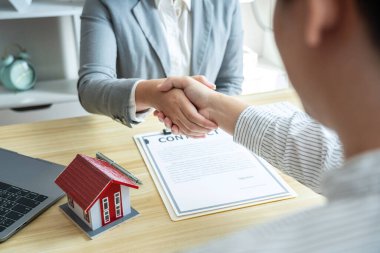 Emlakçı ve müşteriler el sıkışıyor. Ev sigortası ve yatırım kredisi sözleşmesi imzalandıktan sonra bitirilen sözleşmeyi kutluyorlar..