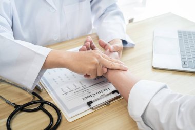 Hastanedeki muayene sırasında beyaz önlüklü doktor hastanın nabzını kontrol ediyor..