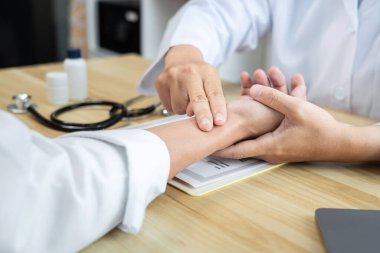 Hastanedeki muayene sırasında beyaz önlüklü doktor hastanın nabzını kontrol ediyor..