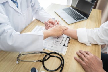 Hastanedeki muayene sırasında beyaz önlüklü doktor hastanın nabzını kontrol ediyor..