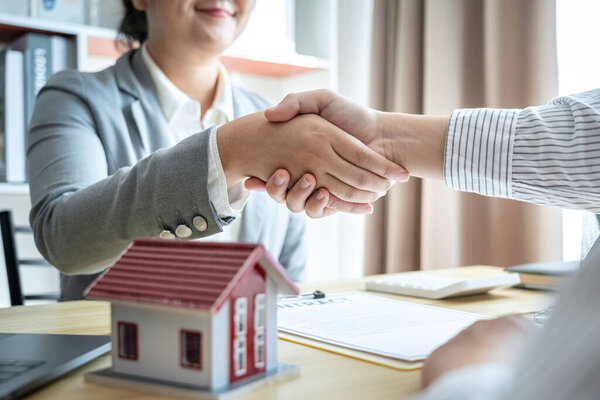Estate agent and customers shaking hands together celebrating finished contract after signing about home insurance and investment loan.