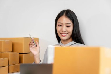 Kadın girişimci, evdeki çevrimiçi alışverişte çalışırken müşteriye teslimat için paket kutularına ürünleri paketlemeden önce tablet üzerindeki müşteri siparişini kontrol ediyor ve bilgi yazıyor