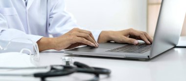 Bir kadın doktor, hasta hastalığının teşhisi için çalışırken ve kliniğinde reçete yazarken dizüstü bilgisayarında hastaların semptomları ve tedavi yöntemleri hakkında yazıyor.