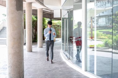 Genç iş adamı elinde kahve fincanı tutuyor ve ortağıyla konuşurken akıllı telefon kullanıyor. Bu cep telefonunu e-postaları kontrol etmek için kullanıyor.