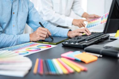 Takım grafik tasarımcısı birlikte yeni proje hakkında beyin fırtınası yapmak için renk şeması üzerinde çalışıyor ve ofiste grafik çizmek için dizüstü bilgisayar kullanıyor