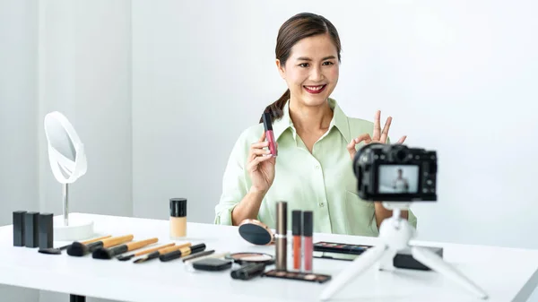 女性の美容ブロガーは 彼女のブログにストリーミングのためのビデオを記録しながら 製品をレビューし 化粧品に使用を示すために口紅を示しています — ストック写真