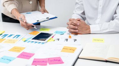 İş kadını elinde belge tutarken ve iş raporunu yöneticiye açıklamaya yönelik tablet üzerindeki verileri gösterirken, patron da yeni başlatılan projeyi dinliyor ve düşünüyor.