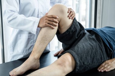 Kadın fizyoterapist tarafından tedavi ve rehabilitasyon için yatağa uzanan erkek hasta, sağlık kliniğinde esneyerek ve fiziksel egzersiz yaparak kadın fizyoterapistten yaralı diz ve bacakları tedavi görüyor.