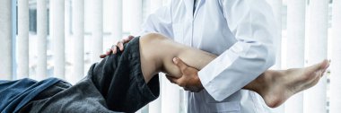 Kadın fizyoterapist tarafından tedavi ve rehabilitasyon için yatağa uzanan erkek hasta, sağlık kliniğinde esneyerek ve fiziksel egzersiz yaparak kadın fizyoterapistten yaralı diz ve bacakları tedavi görüyor.
