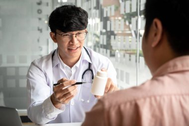 Klinikte yeni bir ilaç ve tavsiye tedavisi hakkında konuşurken, teşhis konulduktan sonra hastalara tıbbi özellikler ve uyuşturucu kullanımını tavsiye etmek üzere ilaç şişesini işaret eden erkek doktor