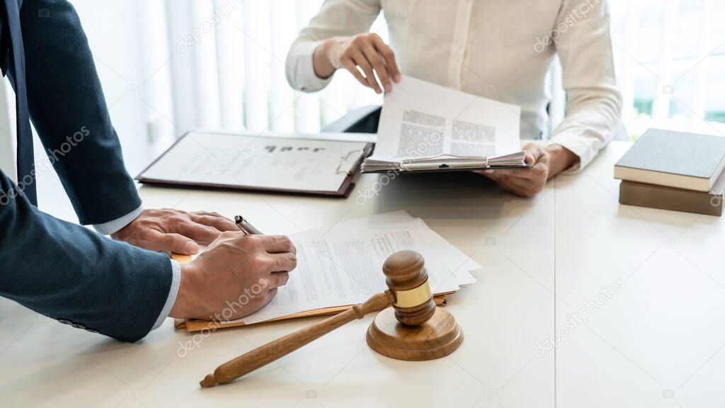 Male lawyer is pointing on legal document to explaining about consultation terms and condition to businesswoman before signing on contract at law firm.