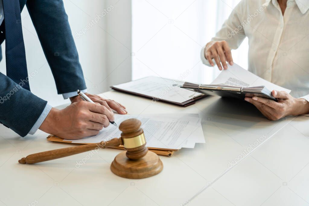 Male lawyer is pointing on legal document to explaining about consultation terms and condition to businesswoman before signing on contract at law firm.