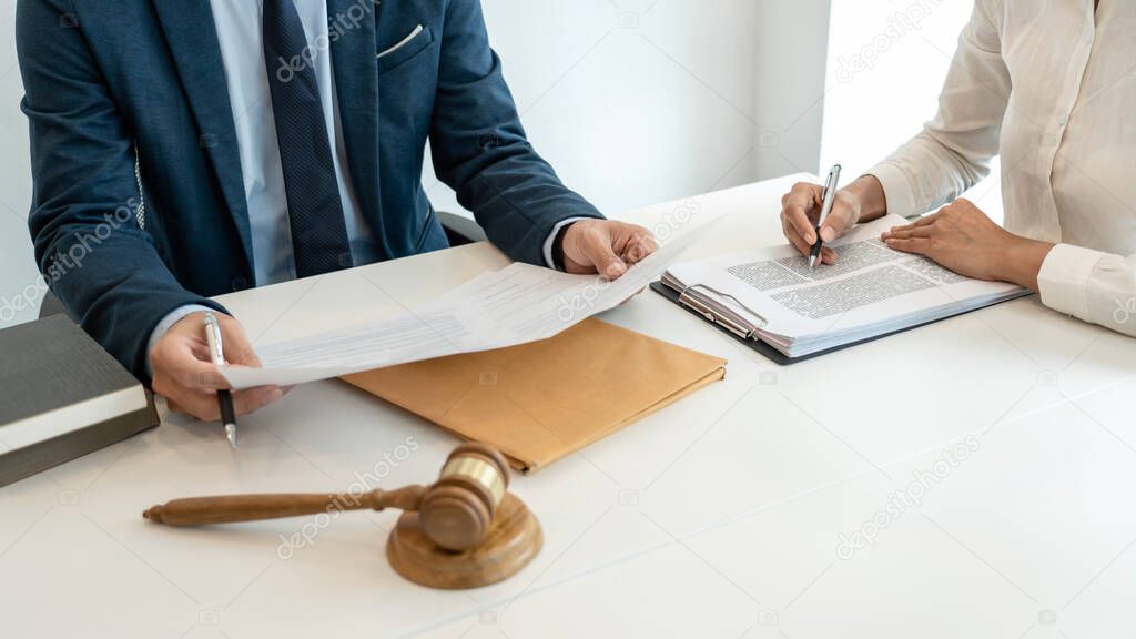 Male lawyer is pointing on legal document to explaining about consultation terms and condition to businesswoman before signing on contract at law firm.