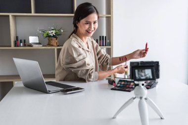 Mutlu gülümseyen zarif kadın ya da video kaydında fırçasıyla güzellik blogcusu. İnceleme ürünü kamera ekranında video blogları hakkında özel ders hazırlıyor..