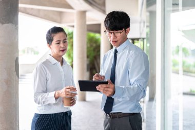 Genç iş ortağı, elinde kahve fincanı tutarken ve bu tableti yatırım planlamaya bakarken iş projesi hakkında konuşmak için tablet kullanıyor.
