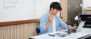 Erkek öğretmen, matematik denklemlerini ve öğrenci öğrenme kursunda fizik formülünü açıklarken webcam 'de video konferansında yeni dersler vermek için dizüstü bilgisayar ve kamera kullanıyor.