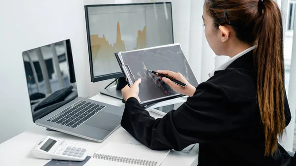 女商人正在用股票数据表来记录和核对笔记本电脑屏幕上的股票交易数据 同时坐在那里分析办公室里的股票交易情况 — 图库照片