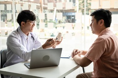 Erkek doktor, klinikte tedavi yöntemleri önerirken teşhis konulduktan sonra hastalığın belirtilerini açıklarken, hastayla tartışıyor..