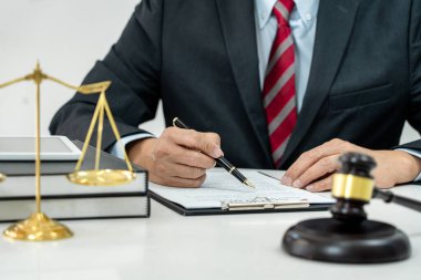 Sözleşme kağıtları, kitap ve ahşap tokmakla çalışan bir erkek avukat veya noter mahkeme salonunda, hukuk ve hukuk hizmetleri kavramında masaya oturur..