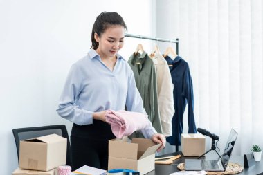 Moda tasarımcısı kadın tasarımcısı ürünleri satmak ve çevrimiçi sipariş almak için canlı yayın videosu yayınlıyor ve evdeki müşteriye teslimat için giysileri paketleyip kutulara koyuyor..