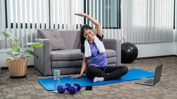 スポーツウェアの女性は 休日に自宅の屋内リビングルームでヨガの練習を行うためにマットに座っている居心地の良い リラックスして健康的なコンセプト — ストック写真