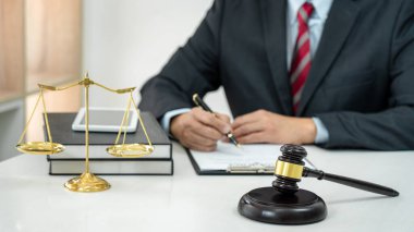 Sözleşme kağıtları, kitap ve ahşap tokmakla çalışan bir erkek avukat veya noter mahkeme salonunda, hukuk ve hukuk hizmetleri kavramında masaya oturur..