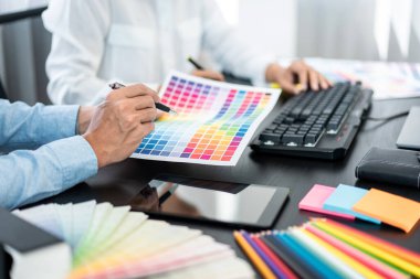 Takım grafik tasarımcısı yeni proje hakkında beyin fırtınası yapmak için renk tablosu üzerinde çalışıyor ve ofiste birlikte çalışmak için dizüstü bilgisayar kullanıyor.