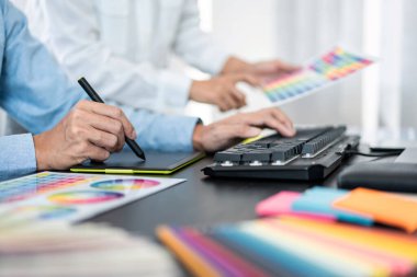 Takım grafik tasarımcısı birlikte yeni proje hakkında beyin fırtınası yapmak için renk şeması üzerinde çalışıyor ve ofiste grafik çizmek için dizüstü bilgisayar kullanıyor