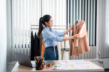 Çalışan ve düşünen kadın moda tasarımcısı atölyede yeni kıyafet koleksiyonu ürünü yapmak için renk örnekleri ve kumaş seçmeye karar verdi.