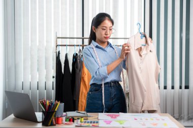 Çalışan ve düşünen kadın moda tasarımcısı atölyede yeni kıyafet koleksiyonu ürünü yapmak için renk örnekleri ve kumaş seçmeye karar verdi.