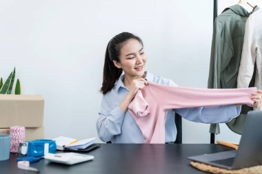 Moda tasarımcısı kadın tasarımcısı ürünleri satmak ve çevrimiçi sipariş almak için canlı yayın videosu yayınlıyor ve evdeki müşteriye teslimat için giysileri paketleyip kutulara koyuyor..