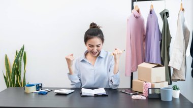 Moda tasarımcısı kadın ürünleri satar ve müşteriden sipariş alır ve müşteriye eve teslimat için kıyafet paketlerini kutulara doldurur..
