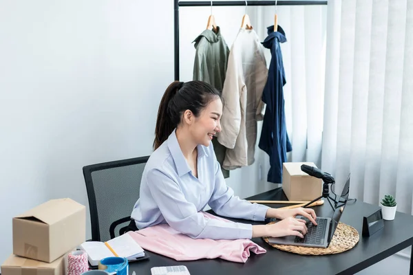 Moda tasarımcısı kadın tasarımcısı ürünleri satmak ve çevrimiçi sipariş almak için canlı yayın videosu yayınlıyor ve evdeki müşteriye teslimat için giysileri paketleyip kutulara koyuyor..