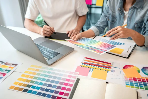 職場で新しいコレクションを作成するためにインスピレーションで選択着色のためのカラースウォッチサンプルチャートに取り組んで創造的なグラフィックデザイナーのチーム — ストック写真
