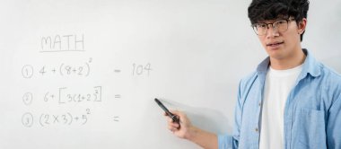 Erkek öğretmen beyaz tahtanın önünde duruyor ve canlı yayın videosuyla e-öğrenme sınıfında konuşurken yeni bir dersi açıklamak için bordaya matematik denklemleri yazıyor.