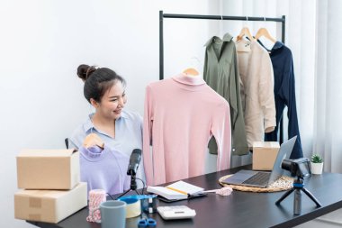 Moda tasarımcısı kadın tasarımcısı ürünleri satmak ve çevrimiçi sipariş almak için canlı yayın videosu yayınlıyor ve evdeki müşteriye teslimat için giysileri paketleyip kutulara koyuyor..