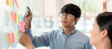 İki işletme yöneticisi, ofiste birlikte pazarlama planının planlanmasına yönelik yeni bir iş projesi hakkında fikir alışverişinde bulunmak için kilit noktayı duvara yazıp not alıyorlar..