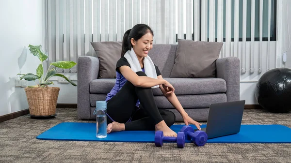 Woman in sportswear is sitting on a mat to do yoga exercise in the indoor living room at home, relaxing and healthy concept.
