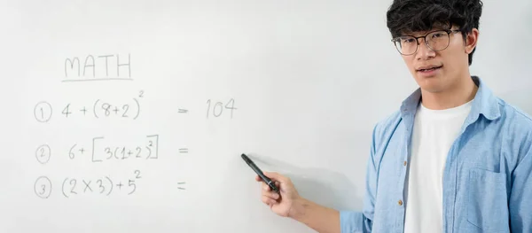 Male tutor standing in front of whiteboard and writing math equations on board to explaining new lesson while talking on e-learning class online by live streaming video