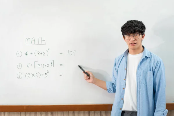 Male tutor standing in front of whiteboard and writing math equations on board to explaining new lesson while talking on e-learning class online by live streaming video