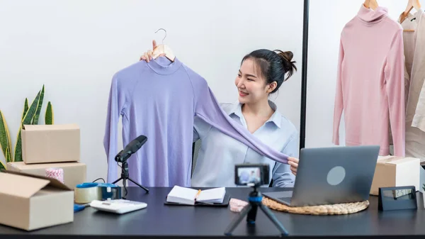 Women fashion designer stylist broadcast live streaming video to sale product and receive online order from customer and prepare packing clothes into boxes for sending delivery to client at home.