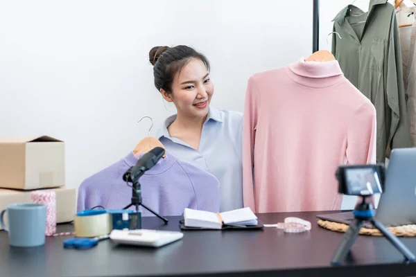 Women fashion designer stylist broadcast live streaming video to sale product and receive online order from customer and prepare packing clothes into boxes for sending delivery to client at home.