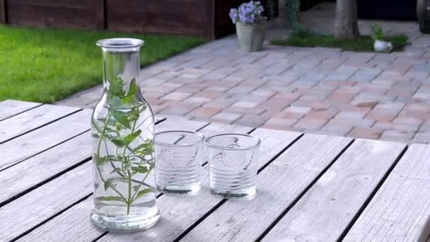 Fles fris water met muntblaadjes op houten tafel op het terras. — Stockvideo