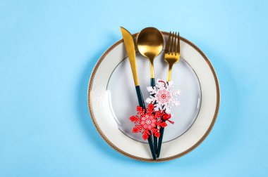 Mavi arka planda modern bulaşık takımı ve süslemeleri olan bir Noel masası. Üst Manzara. Yeni yıl yeri ayarlama. Noel sofra takımı. Noel yeri dekorasyonu. Dekorlu Noel yemeği takımı.