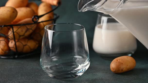 Häll vegansk potatismjölk i glas och potatis i skål på mörk bakgrund. Vegansk mjölk. Växtbaserad mjölkersättning och laktosfri. Vegetabilisk mjölk — Stockvideo