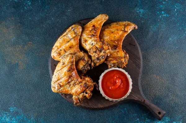 Grilled spicy chicken wings with ketchup on a black plate on a dark slate, stone or concrete background. Top view with copy space. BBQ concept