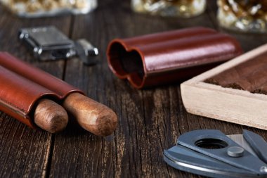 Two Cuban cigars in a leather case with a wooden box on an old brown table top. Glass of whiskey on a blurred background. clipart