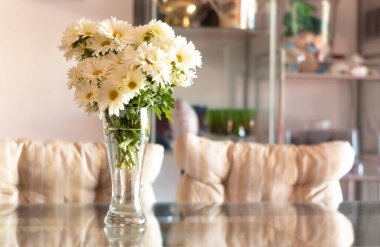 Bouquet of daisies, in a glass vase, on a table in a bright and modern living room. Home decoration and interior. Springtime concept. Copy space